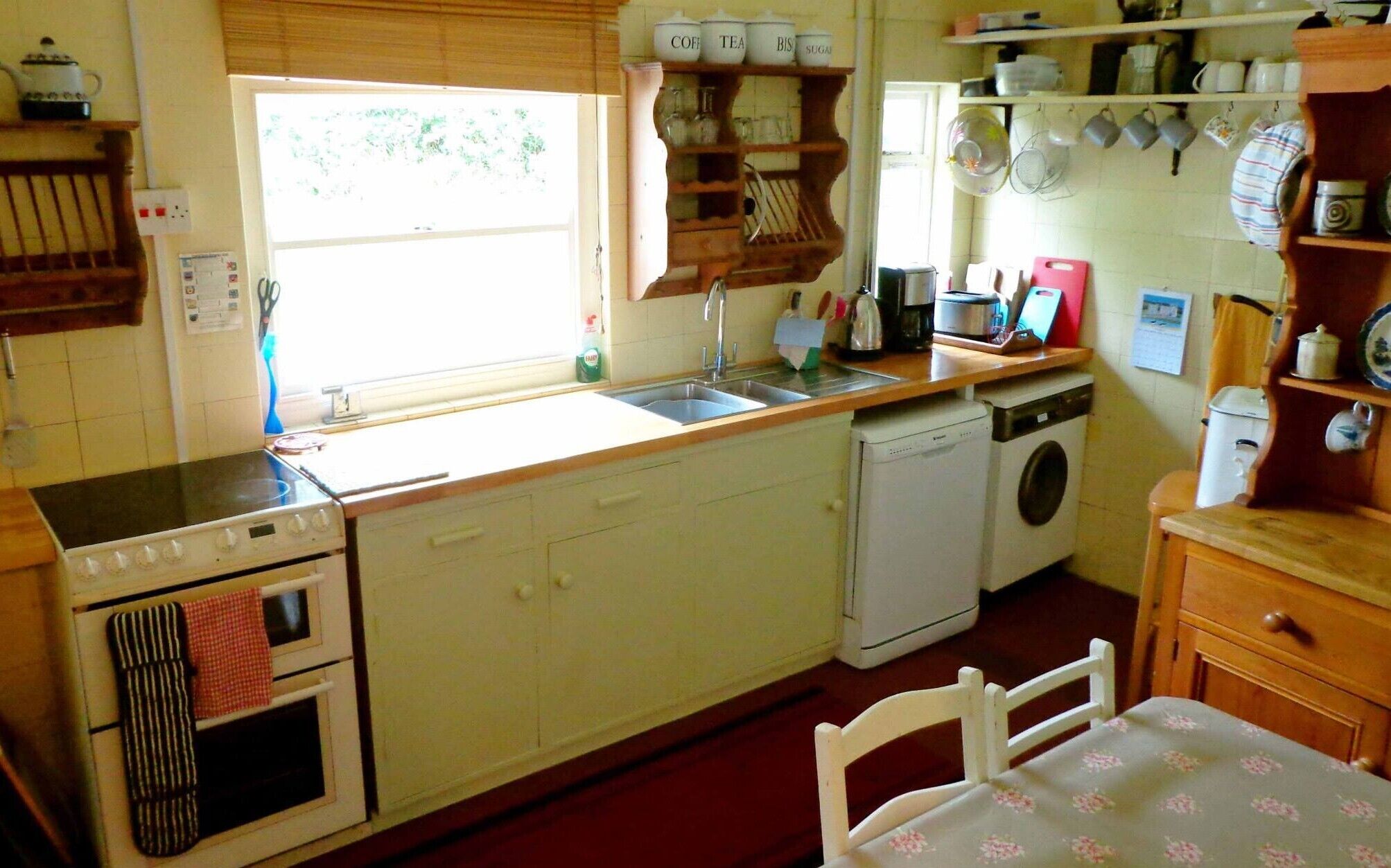 A kitchen with a stove, oven, sink, and dishwasher. There are shelves above the sink with jars and a coffee maker.