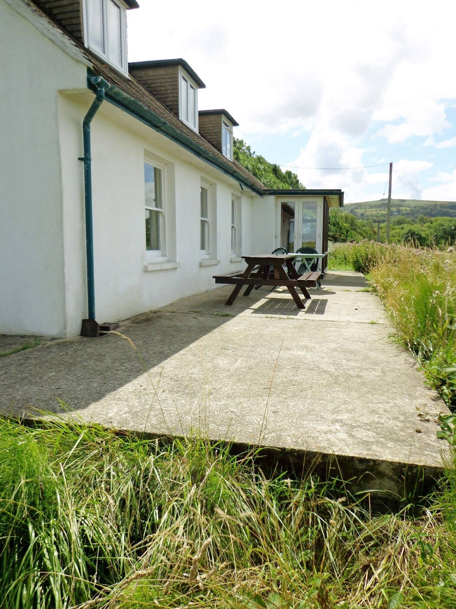 Ein weißes Gebäude mit einer Beton-Terrasse, einem Picknicktisch und einer kleinen Schutzhütte.