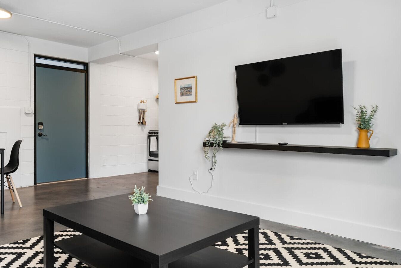 Un salon moderne avec une table basse noire, un téléviseur fixé au mur et une étagère ornée d’objets décoratifs.
