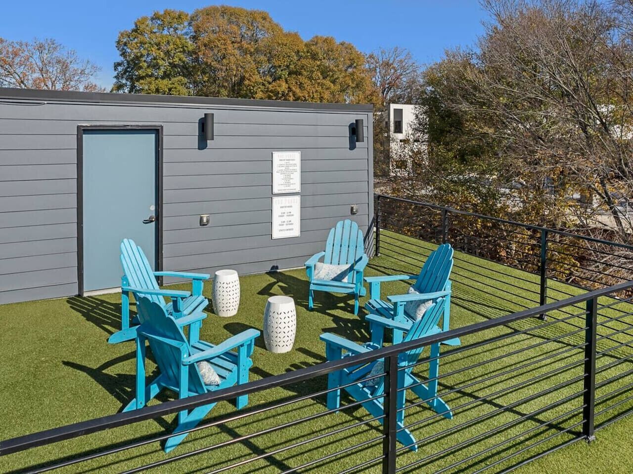 A small building with a door and windows, surrounded by artificial grass and blue chairs.