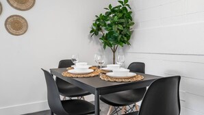 Un comedor con una mesa dispuesta para cuatro personas, sillas negras y individuales de fibras naturales.