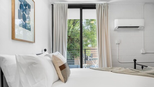 Habitación de hotel con cama, ventana con cortinas, aire acondicionado y vista a zonas verdes.