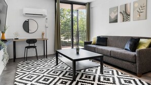 Una sala moderna con un sofá gris, un espejo redondo, una mesa de comedor con una silla y una alfombra estampada.