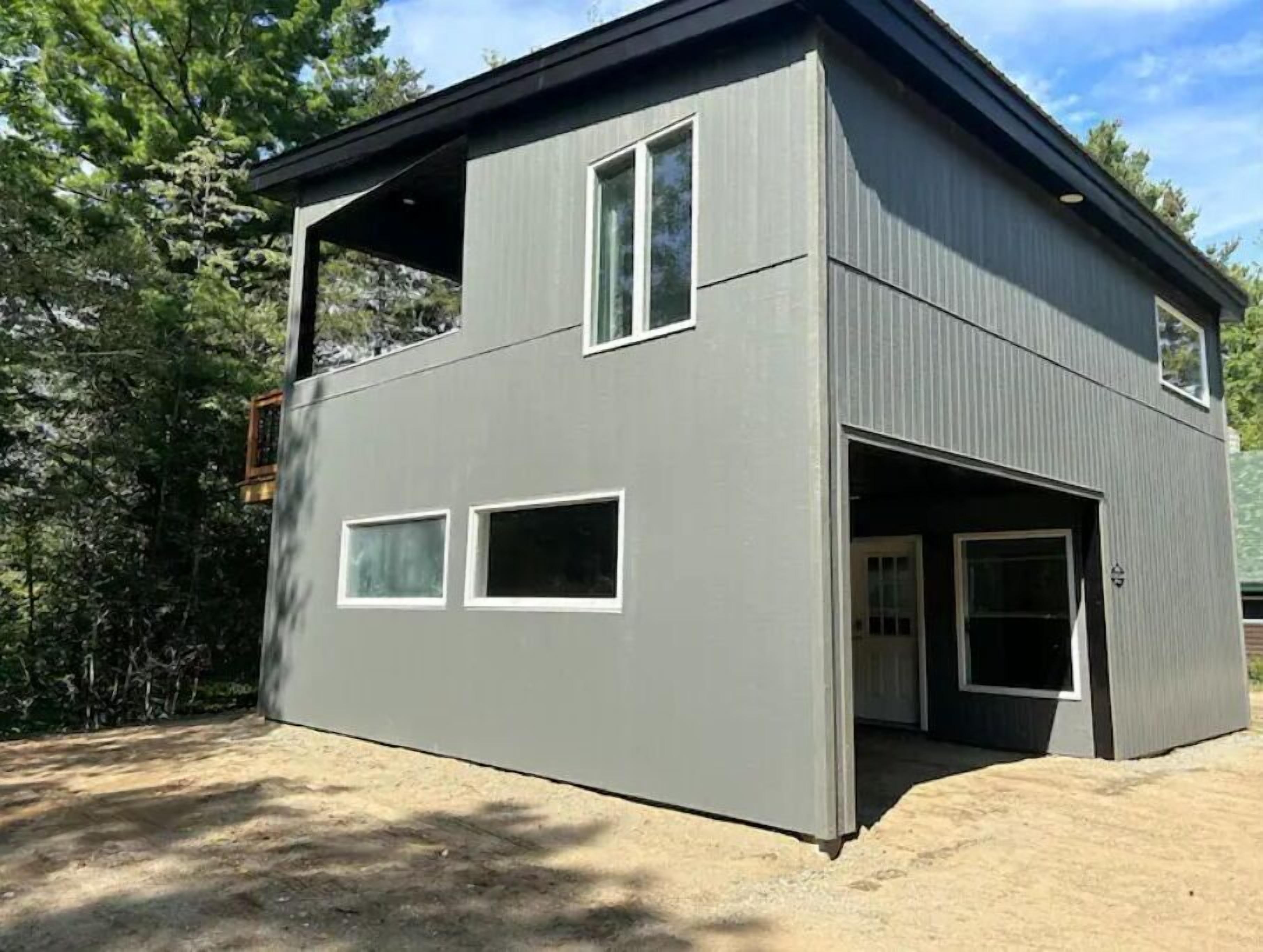 A two-story building with a garage door, large windows, and a sloped roof.