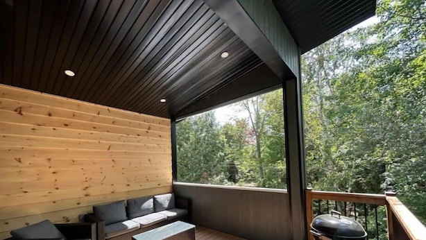A covered outdoor seating area with a wooden deck, a sofa, a bench, and a grill. - Ski, Bike and family fun at "The Future" cottage.  (Jay)