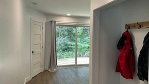 A hallway with a wooden floor, a white door, and a sliding glass door leading to a balcony with a view of greenery. - Ski, Bike and family fun at "The Future" cottage.  (Jay)