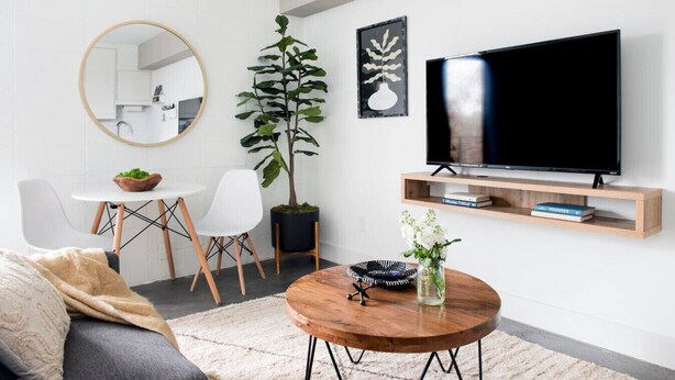 A modern living room with a round wooden coffee table, a sofa, a dining table with chairs, a large potted plant, a flat-screen TV on a wooden stand, and a mirror on the wall. - * NEW * - The Marigold: Private Balcony | Walkable (Atlanta)