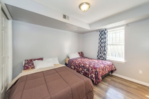 Un dormitorio con dos camas, una ventana con cortinas estampadas y una lámpara en el techo.