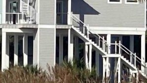 A two-story beachfront house with a balcony, a staircase leading to the main entrance, and a sandy beach in the foreground. - SandyFeet Beach House Retreat-Gulf Front Home at Shell Point Beach.  (Crawfordville)