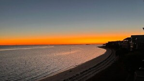A beach with a clear sky at sunset, a sandy shore, and buildings along the coastline. - SandyFeet Beach House Retreat-Gulf Front Home at Shell Point Beach.  (Crawfordville)