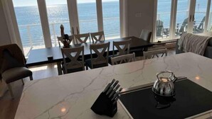 A kitchen with a large island, dining area with chairs, and a view of the sea through large windows. - SandyFeet Beach House Retreat-Gulf Front Home at Shell Point Beach.  (Crawfordville)