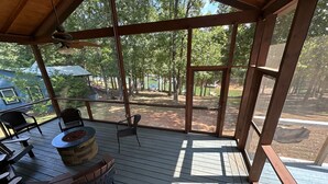 Eine überdachte Terrasse mit Holzboden, einem Steinkamin und Metallstühlen.