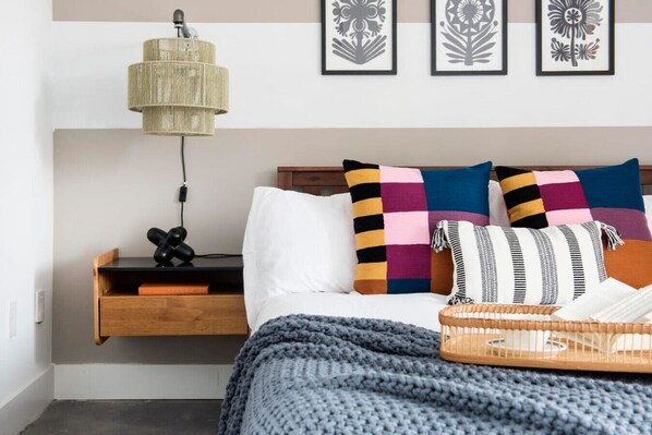 Une chambre bien rangée, avec un lit, une table de chevet dotée d’une lampe et une étagère fixée au mur.