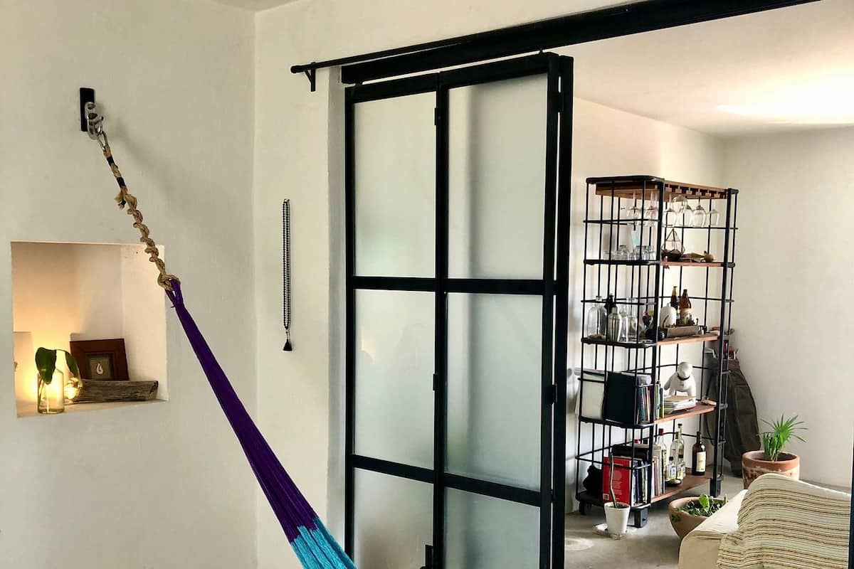A room with a bed, a hammock, a sliding door, and a shelving unit with various items.