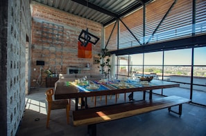 A dining area with a long table set for a meal, a brick wall, and a view through large windows. - Casas del Obraje (San Miguel de Allende)