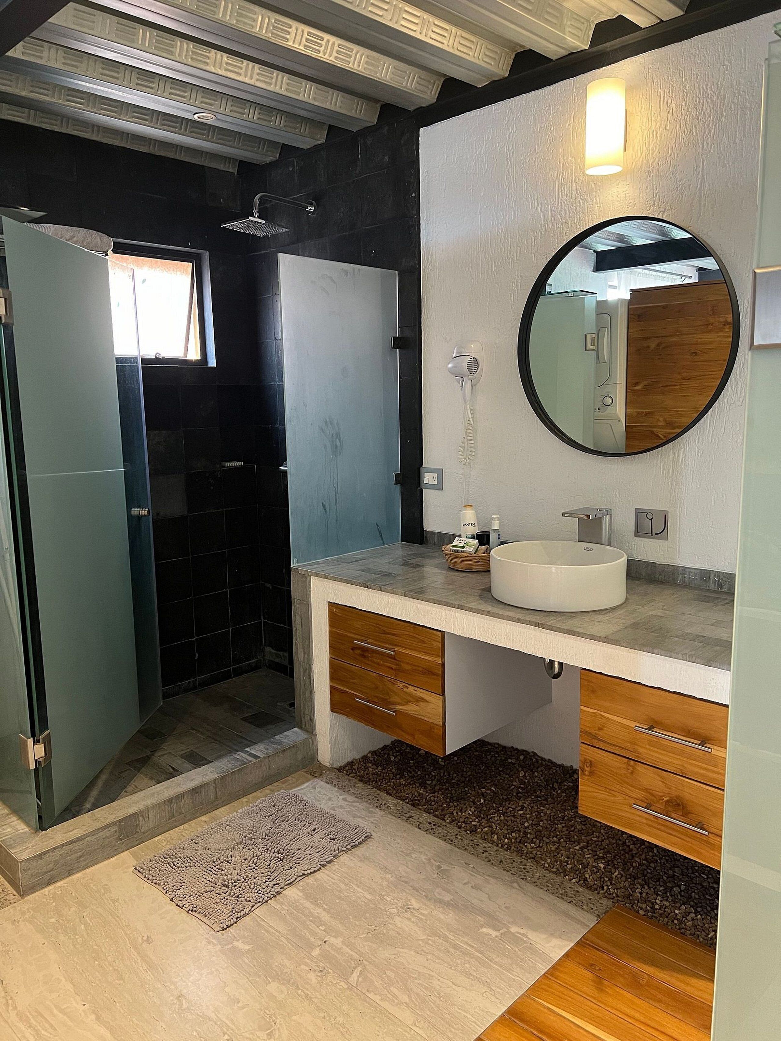 A modern bathroom with a glass shower enclosure, a vanity with a sink, and a round mirror.