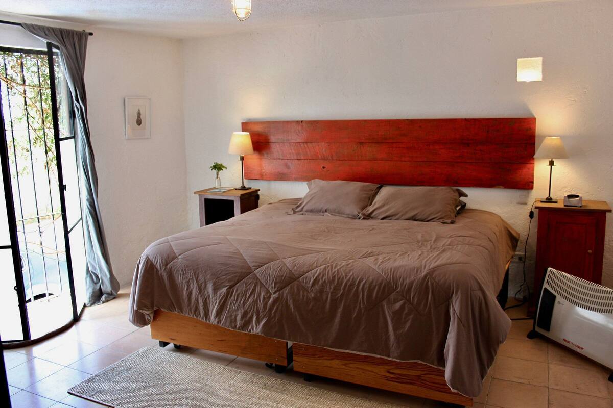 A bedroom with a bed, bedside lamps, a nightstand, a radiator, and a view through a door.