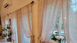 Una habitación con piso de madera, cortinas color beige y una ventana con un jarrón de flores.