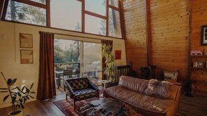 Ein gemütliches Wohnzimmer mit Ledersofa, Couchtisch mit Muster und großem Fenster mit Blick auf eine Terrasse.
