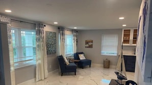 A spacious living room with a marble floor, two blue armchairs, a small table, and a decorative wall piece.