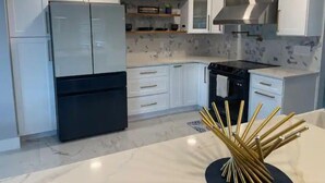A modern kitchen with white cabinets, a black refrigerator, a built-in stove, and a marble countertop.