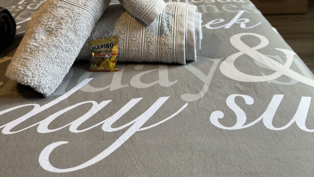 A neatly made bed with a grey and white patterned bedspread, a small bedside table with a lamp, and several rolled towels. - Schön, Modern und Ruhige Lage. Nah am Zentrum Perfekt für 4. Parking, Netflix (Arona)