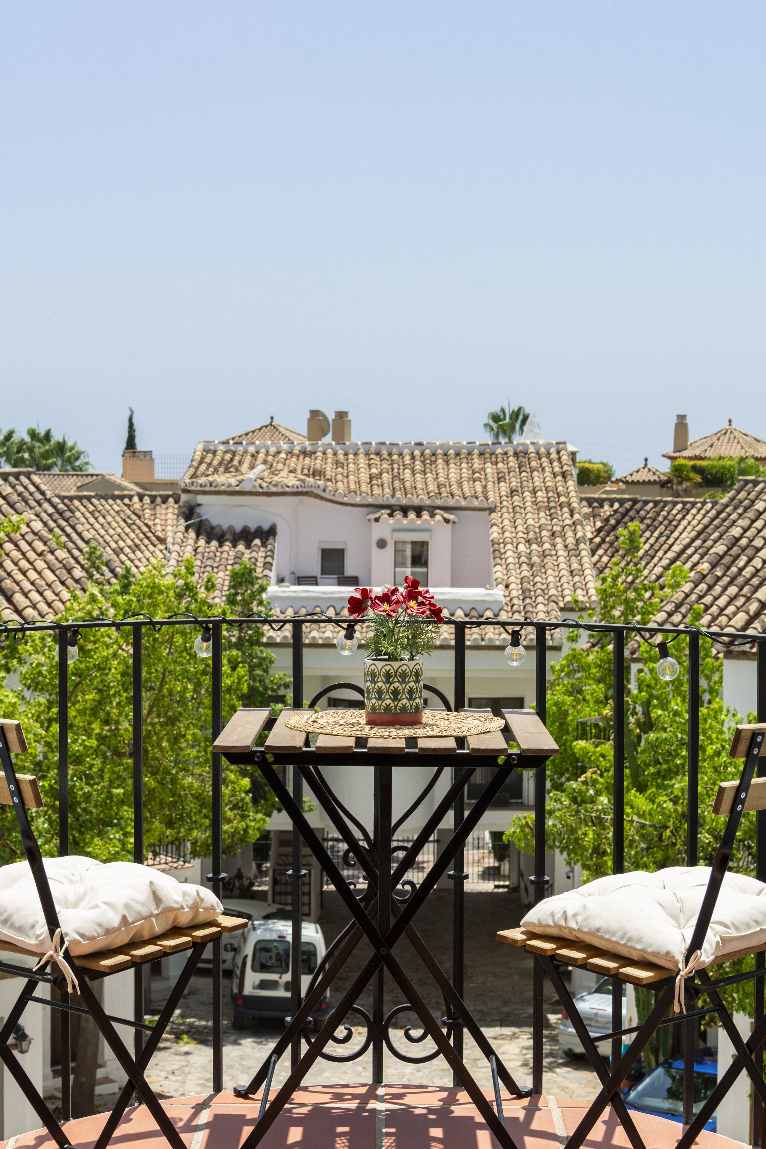 Un balcon avec une table, deux chaises et un pot de fleurs.