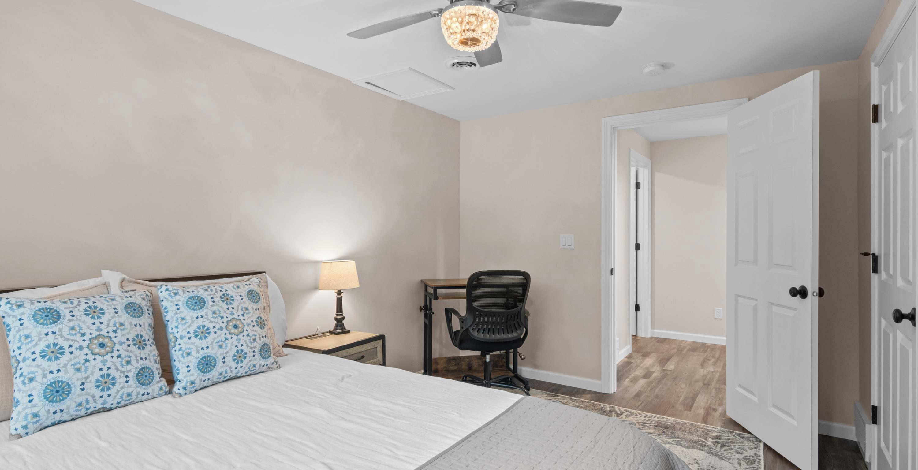 Quarto com cama, escrivaninha, cadeira, ventilador de teto e porta.