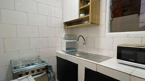 A compact kitchen with white tiled walls, a gas stove, a microwave, and black cabinets. - Merryhome, Studio Avec bcp de Charme (Abidjan)