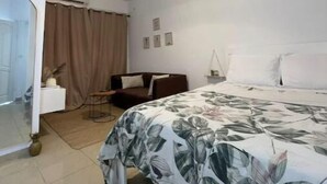 A hotel room with a bed, a sofa, a small table, and a hanging light fixture. - Merryhome, Studio Avec bcp de Charme (Abidjan)