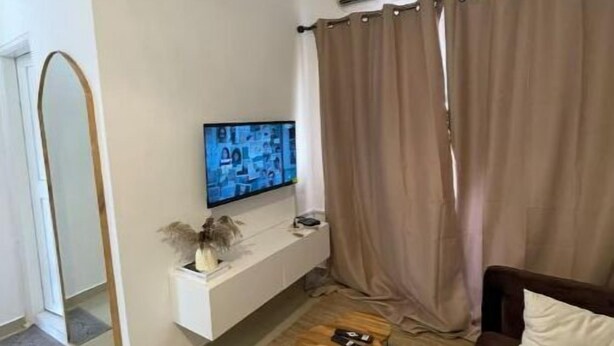 A living room with a TV on a white stand, a brown sofa, a wooden coffee table, and a large mirror. - Merryhome, Studio Avec bcp de Charme (Abidjan)