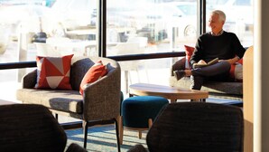 Un espacio lounge moderno con asientos cómodos, ventanas amplias y vistas a coches estacionados afuera.