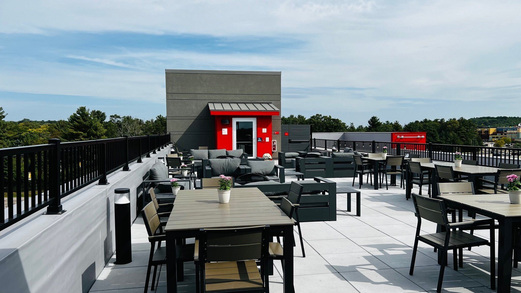 An outdoor seating area with tables and chairs, a red building in the background, and a clear sky.