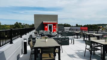 Un espacio al aire libre con mesas y sillas, un edificio rojo al fondo y un cielo despejado.