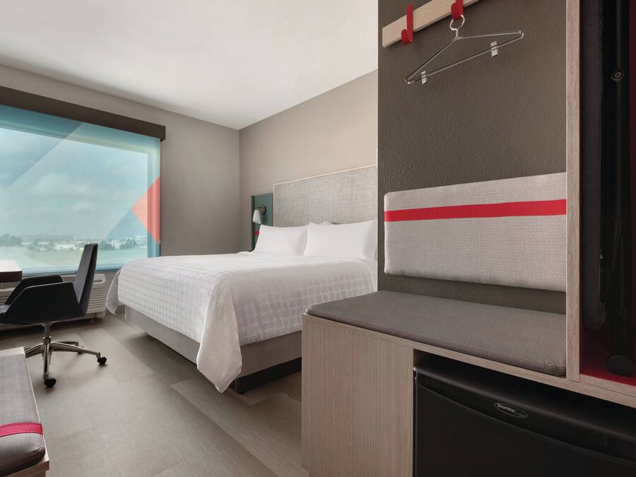 A hotel room with a bed, desk, chair, and a view of the city.
