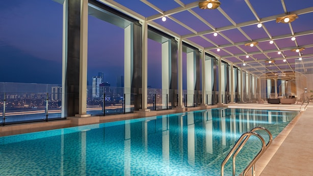 Piscina interior moderna com paredes de vidro transparente, vista para a cidade e design contemporâneo.