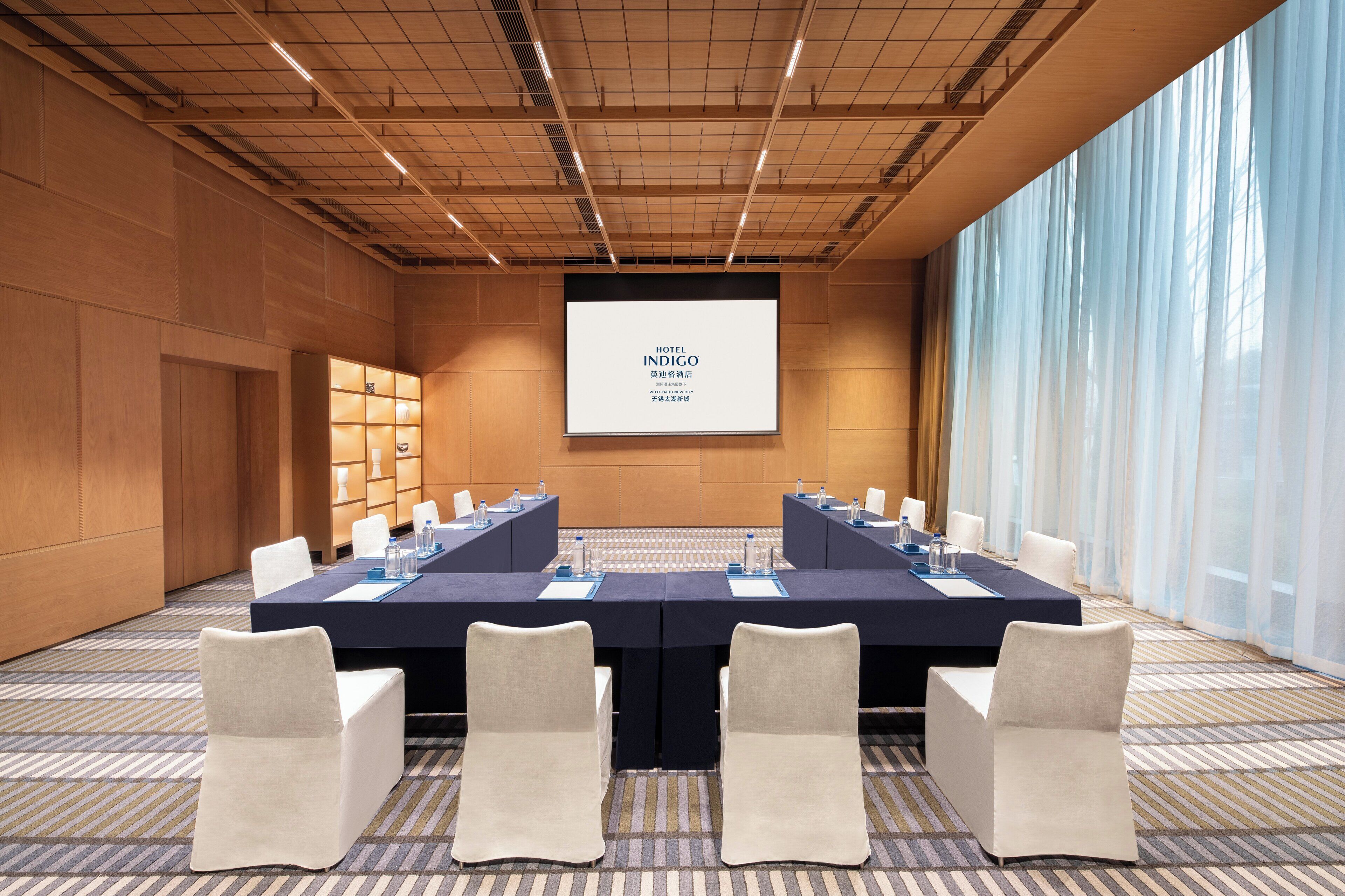 A conference room with a long table, chairs, and a projection screen displaying "HOTEL INDIGO".
