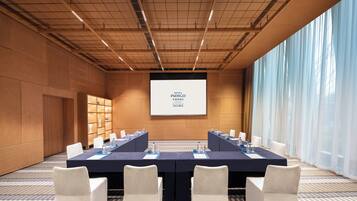 Une salle de conférence avec une longue table, des chaises et un écran de projection affichant le texte « HÔTEL INDIGO ».
