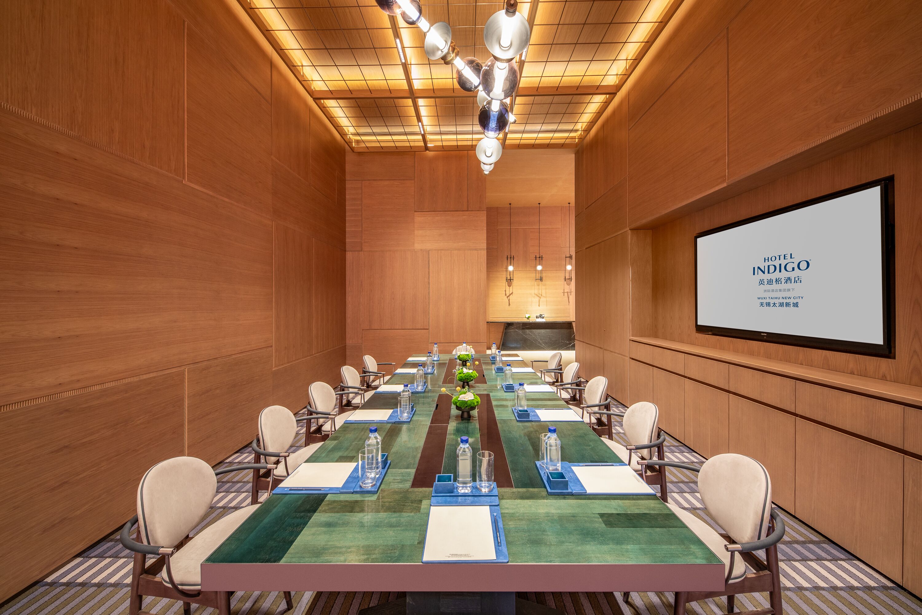 Une salle de conférence avec une longue table, des chaises, un écran de projection et un mur recouvert de panneaux en bois.