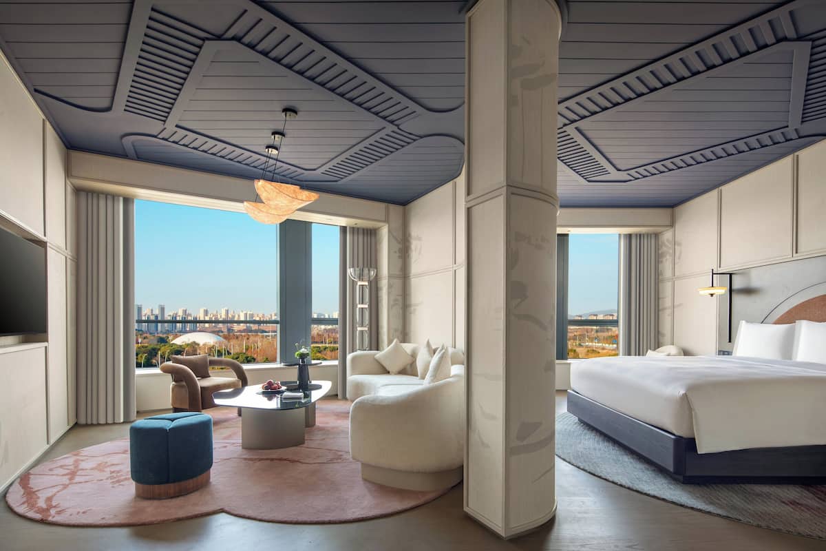 Ein modernes Hotelzimmer mit einem großen Bett, einer Couch, einem Couchtisch und Blick auf die Stadt.