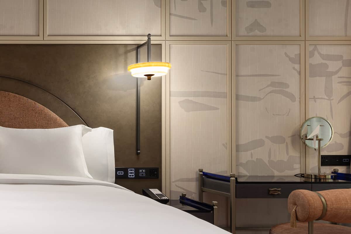 Ein Hotelzimmer mit Bett, Nachttisch, Lampe, Spiegel und einem Sessel.