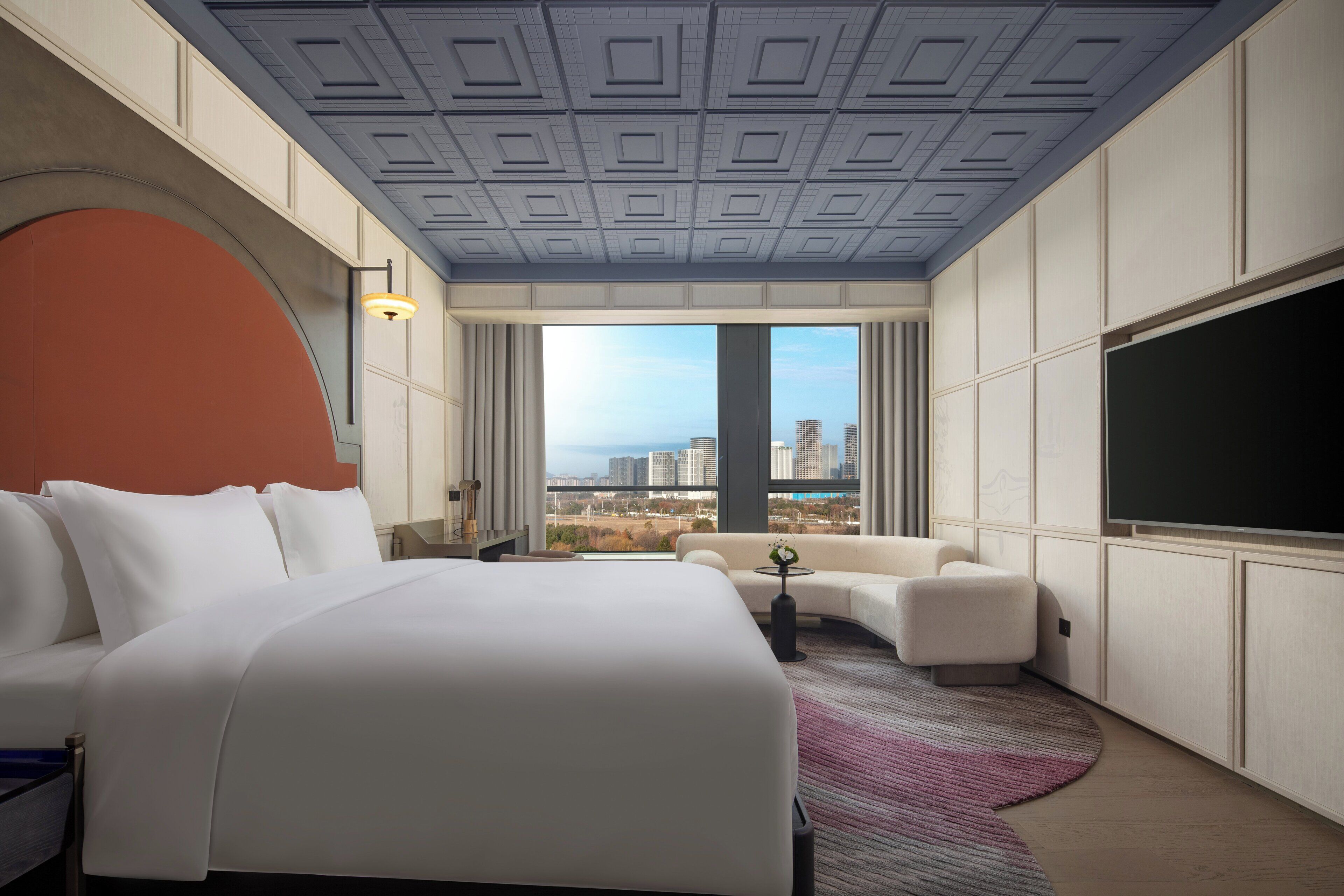 Una habitación de hotel moderna con una cama grande, un sofá, un televisor y vistas a la ciudad.