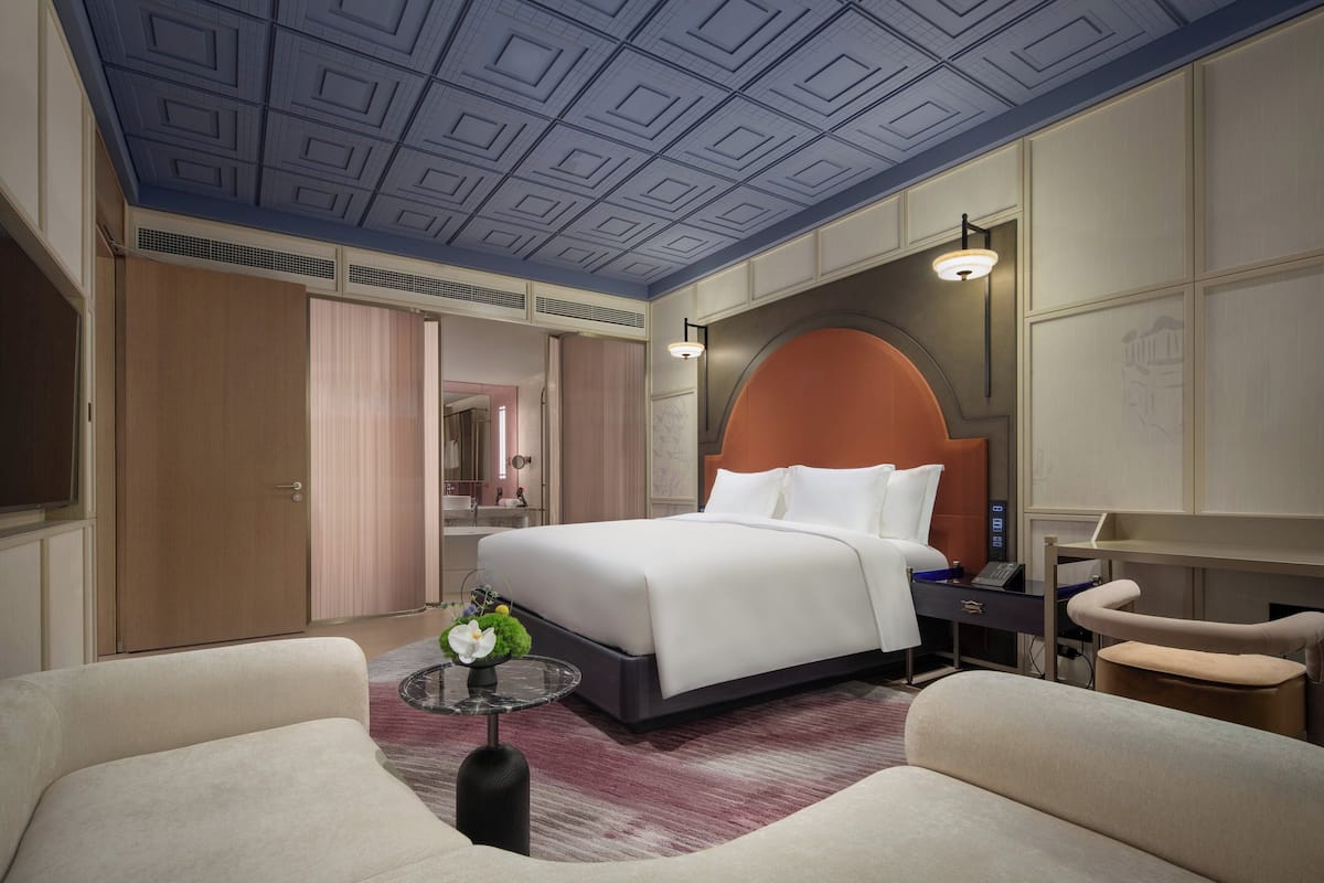 Ein Hotelzimmer mit einem großen Bett, einem Schreibtisch, einem Stuhl und einem kleinen Tisch mit einer Blumenvase.