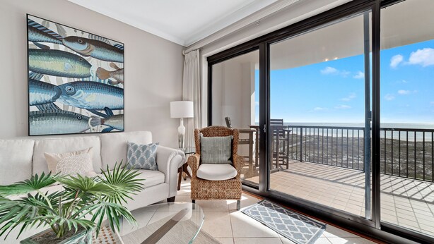 A modern living room with a large window, a sofa, a chair, and a glass coffee table. - Grande Pointe 414 | Beach, Pools, Fitness Center | My Beach Getaways (Orange Beach)