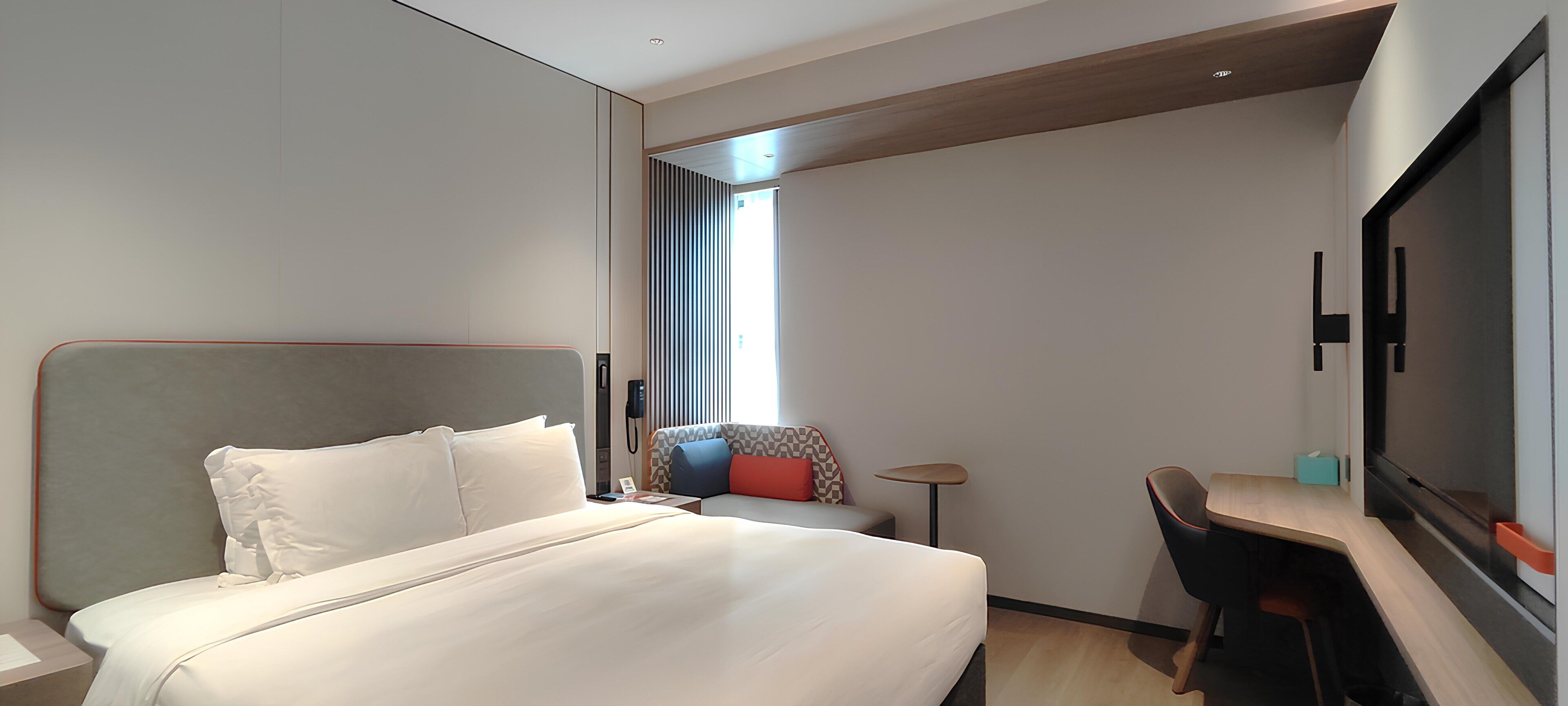 A hotel room with a large bed, a desk, a chair, a TV, and a window with blinds.