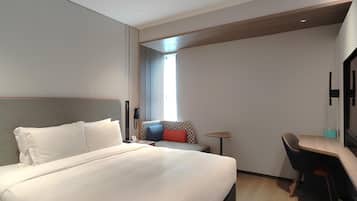 A hotel room with a large bed, a desk, a chair, a TV, and a window with blinds.