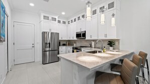 Una cocina moderna con armarios blancos, electrodomésticos de acero inoxidable, una isla de mármol y taburetes de bar.