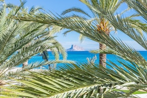 A beach view with palm trees and a rocky outcrop in the distance.
