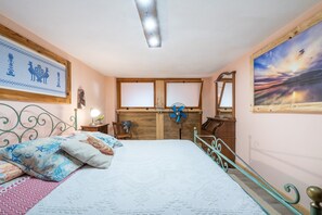 Un dormitorio con cama, cabecera de madera, ventilador de pared, mesita de noche, cómoda y un cuadro enmarcado.