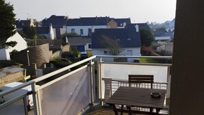 A balcony with a table and chairs, overlooking a residential area with houses and a body of water. - Studio Apartment 'Au Coeur De Quiberon' with Shared Pool, Balcony and Wi-Fi (Quiberon)